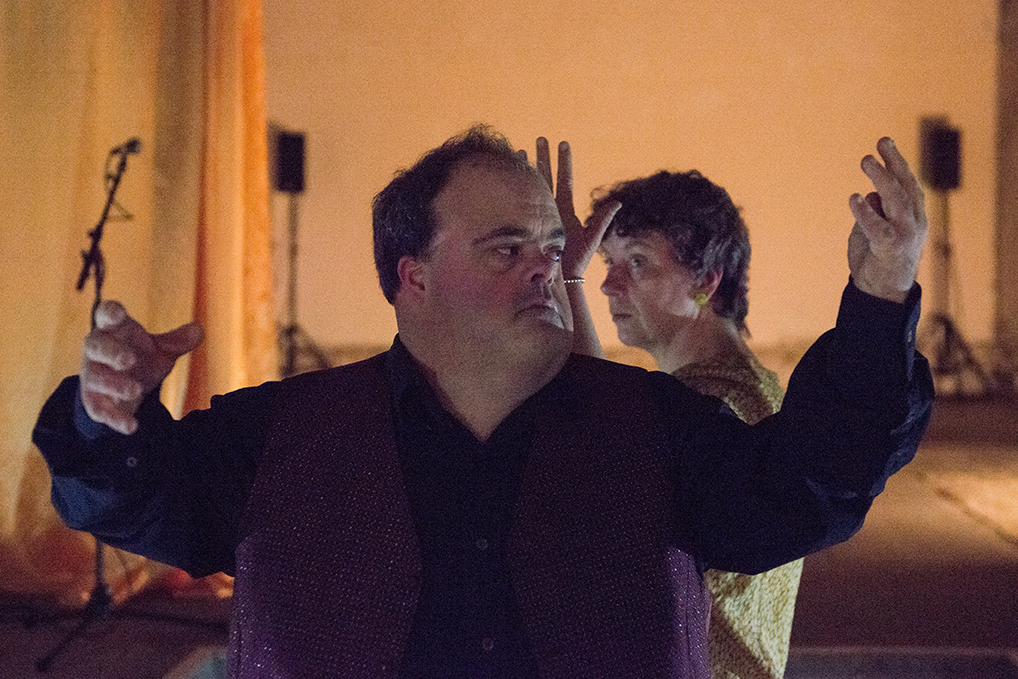 A photo still of the performance Empty Theatre Dream by Corali Dance Company 2014. The photo is taken in Dilston Grove (Café Gallery Projects) and features Graham Evans and Jackie Ryan dancing with their arms raised in a u shape in formation with another, their costumes are burgundy and gold. 